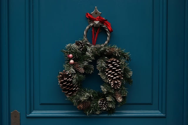 A wreath of pine cones and holly tied with a red ribbon sits on a blue door